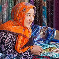 Kyrgyz woman with golden teeth selling colourful fabrics at market in Osh, Kyrgyzstan 