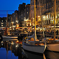 Sailing boats and tourists at pavement cafés / sidewalk cafes along the quay of the Honfleur harbour at night, Normandy, France