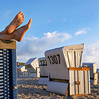 Feet sticking out from roofed wicker beach chair at Sylt, North Frisian Island, Schleswig-Holstein, Germany