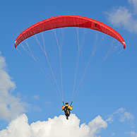 Paraglider in flight with red wing / canopy against blue cloudy sky, Brittany, France